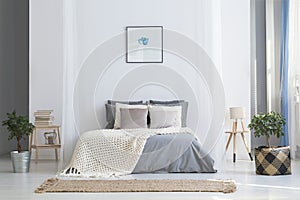 Simple poster above bed with knit blanket in bright bedroom inte