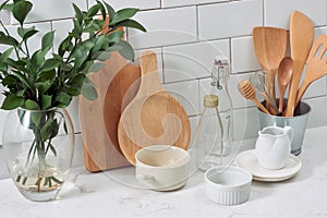 Simple rustic kitchenware against white wooden wall: rough ceramic pot with wooden cooking utensil set, stacks of ceramic