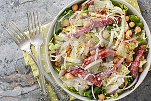 Simple salad combines salami, mozzarella, chickpeas, iceberg lettuce, and romaine, all topped off with a simple red wine photo