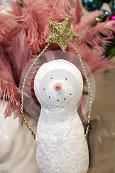 Simple sparkly Christmas snowman decoration holding glitter gold star over its head in front of pink feathers and baubles