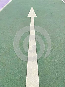 Simple straightforward solution concept: White isolated arrow on green pavement showing direction straight ahead