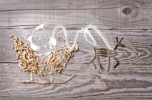 Simple symbols of Father Christmas sleigh arranged from sawdust and reindeer made from dry wooden sticks on wooden grey background