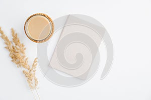 Simple trendy office desk with notebook, cup of coffee and dry reeds on white background. Minimal style feminine workspace
