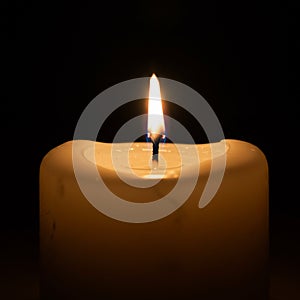 A simple white candle with a lit flame in a dark setting. The candle wax appears