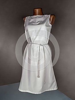 Simple white dress with a belt on a mannequin, isolated on a dark background. Mockup or background for overlaying a pattern on