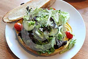 Simple white plate with brunch frittata covered with fresh salad greens