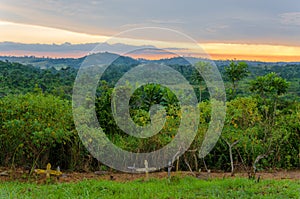 Simple wooden crosses and graves in front of lush jungle and dramatic sunset in Congo