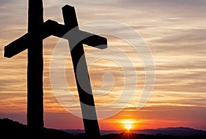 Simple wooden holy cross standing on a hill at sunset, silhouette against the glowing sky. AI generated.