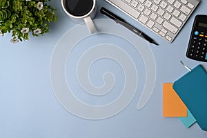 Simple workplace with calculator, notebook, glasses, coffee cup, keyboard and pen on blue background.