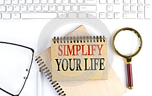 SIMPLIFY YOUR LIFE text in the office notebook with keyboard, magnifier and glasses , business concept