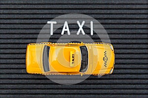 Simply design yellow toy car Taxi Cab model with inscription TAXI letters word on black background. Automobile and transportation