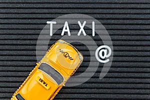 Simply design yellow toy car Taxi Cab model with inscription TAXI letters word on black background. Automobile and transportation