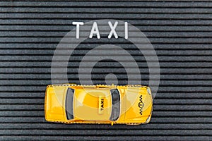 Simply design yellow toy car Taxi Cab model with inscription TAXI letters word on black background. Automobile and transportation