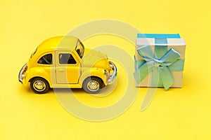 Simply design yellow vintage retro toy car delivering gift box on roof isolated on trendy yellow background. Christmas New Year