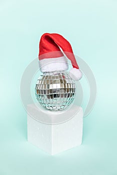 Simply minimal composition disco ball in Santa hat and cube shapes geometric form podium isolated blue pastel background.