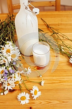 Simply stylish wooden kitchen with bottle of milk and glass on table, summer flowers camomile, healthy food moring