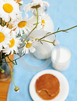 Simply stylish wooden kitchen with bottle of milk and glass on table, summer flowers camomile, healthy food morning