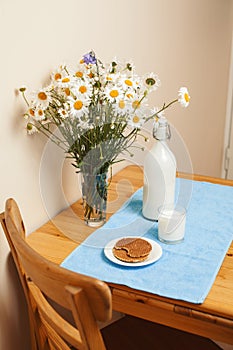 Simply stylish wooden kitchen with bottle of milk and glass on table, summer flowers camomile, healthy foog moring