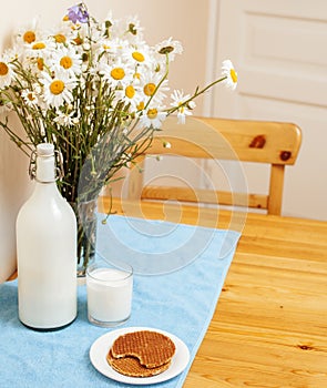 Simply stylish wooden kitchen with bottle of milk and glass on table, summer flowers camomile, healthy foog moring