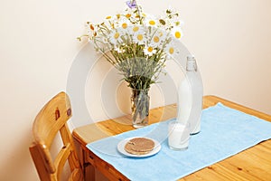 Simply stylish wooden kitchen with bottle of milk and glass on table, summer flowers camomile, healthy foog moring