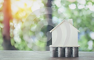 The simulated wooden house rests on a pile of coins and all on the wooden floor.