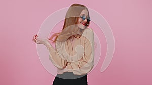 Sincere cool cheerful brunette girl in beige blouse wearing sunglasses, charming smile on pink wall