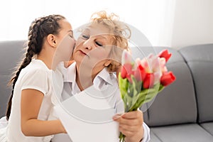Sincere cute little granddaughter strong cuddling and kissing in cheek her 60s grandmother gave her pretty spring