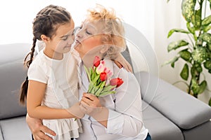 Sincere cute little granddaughter strong cuddling and kissing in cheek her 60s grandmother gave her pretty spring