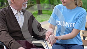 Sincere girl volunteer holding disabled retiree hand, supporting hospice people