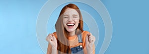 Sincere happy rejocing ginger girl close eyes smiling broadly say yes waving clenched fists joyfully celebrate enterting