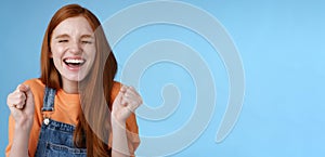 Sincere happy rejocing ginger girl close eyes smiling broadly say yes waving clenched fists joyfully celebrate enterting