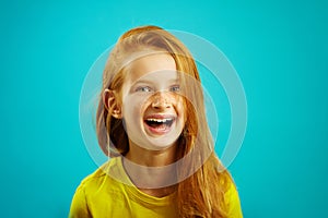 Sincere laughter of children girl with red hair on blue isolated. Happy child expresses a sincere emotion.