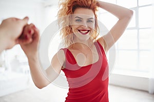 Sincere smile. Attractive woman in red dress and curly hair in the spacey room near the window