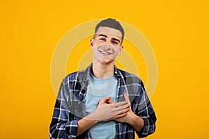 Sincere young guy putting hands on his heart, expressing gratitude on orange studio background