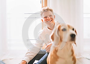 Sincerely laughing young man sitting on the floor with unfocused beagle dog portrait on the foreground