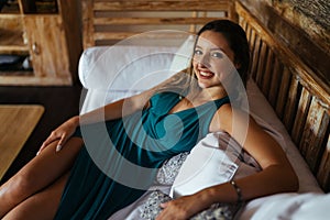 sincerely smiles and looks the incendiary flirtatious look of a girl in a turquoise dress leaning on pillows