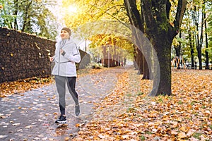 Sincerely smiling athletic woman have a jogging in the autumnal city park. Young fitness female smiling and running by the footway photo