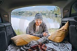 Sincerely smiling middle-aged man dressed in warm knitted clothes and jeans portrait in the cozy car trunk and with beautiful