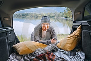 Sincerely smiling middle-aged man dressed in warm knitted clothes and jeans portrait in the cozy car trunk and with beautiful photo