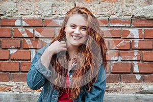 Sincerely smiling Red curled hair caucasian teen girl with blue eyes fashion portrait on the red brick wall background. Natural