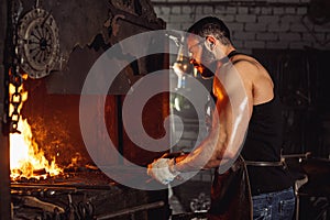 Sinewy young man heating iron in fire