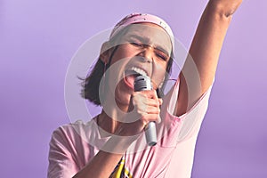 Sing with your soul, not your voice. Studio shot of a beautiful young woman singing with a microphone against a purple