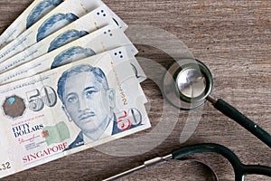 Singapore dollar banknote with stethoscope on woode table.Singapore Healthcare and medical treatment cost and insurance after