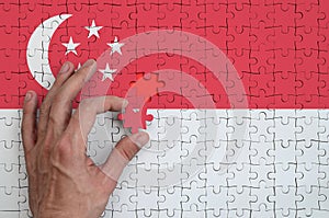 Singapore flag is depicted on a puzzle, which the man`s hand completes to fold