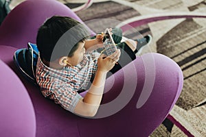 SINGAPORE - June, 2019: Boy playing smartphone in departure lounge at airport