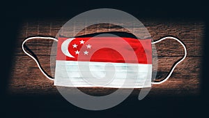 Singapore National Flag at medical, surgical, protection mask on black wooden background. Coronavirus Covidâ€“19, Prevent