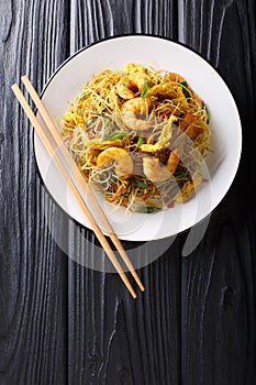 Singapore Noodles Mei Fun with shrimps, sausage, omelet and vegetables close-up on a plate. Vertical top view