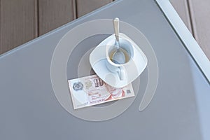 Singapore ten dollars bill and empty cup of coffee on a glass table of outdoor cafe. Payment, tip.