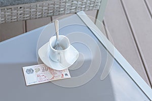 Singapore ten dollars bill and empty cup of coffee on a glass table of outdoor cafe. Payment, tip.