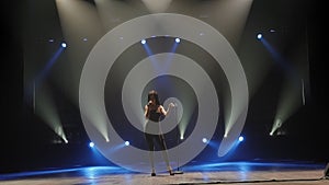 The singer in black suits singing and dancing on stage in the dark with lighting